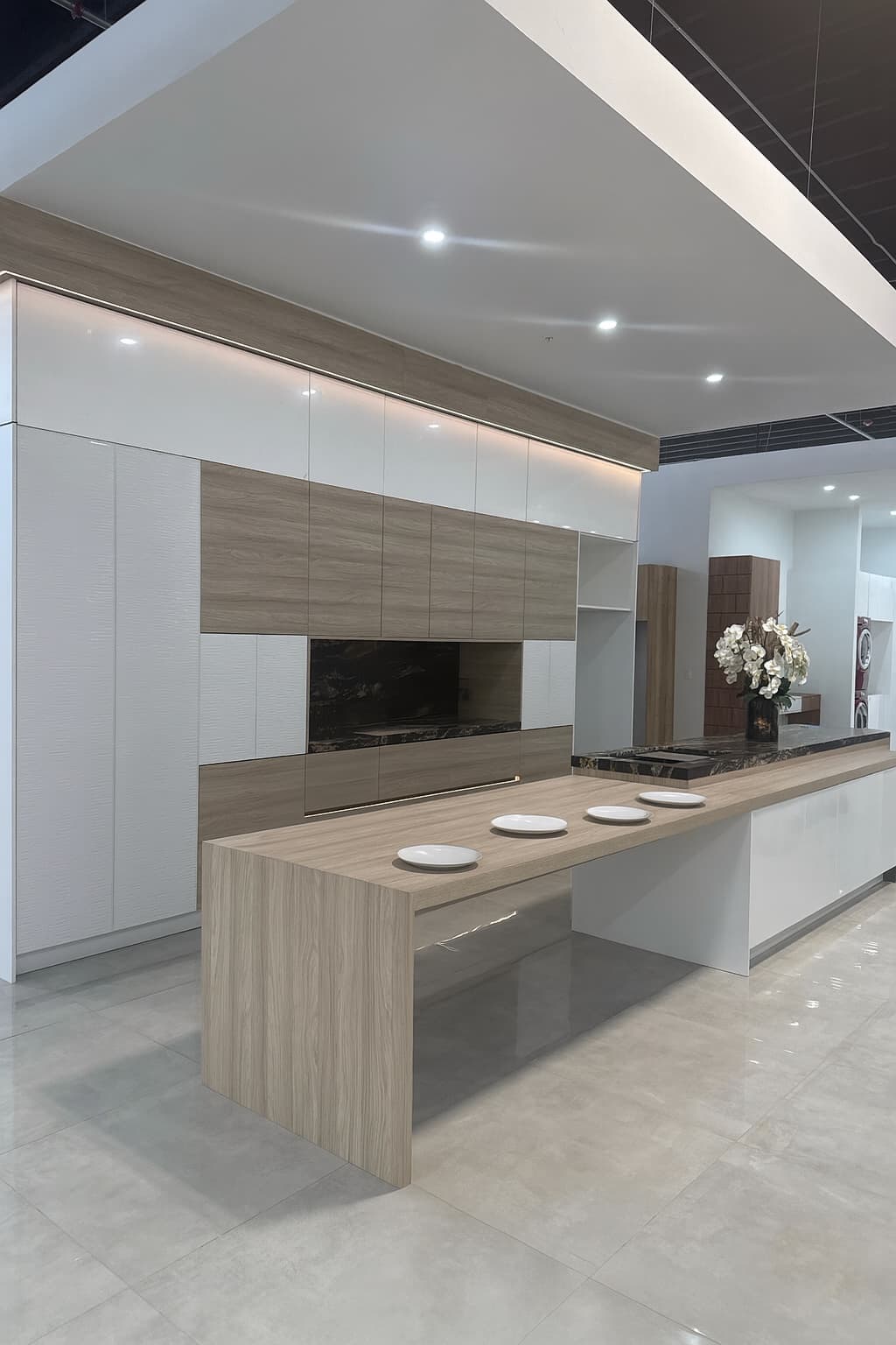 Showroom kitchen with a wall of tall white and oak cabinets and a long oak island set with four plates